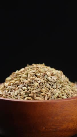 Pile of fennel seeds in brown wooden bowl rotating slowly on balck background, Close-up view