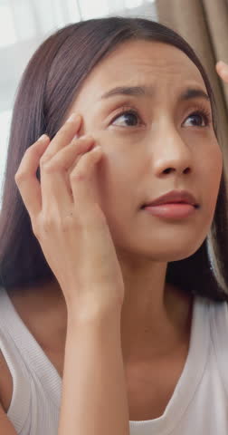 vertical clip. Beautiful Asian woman with tanned skin looking in mirror and checking her facial skin condition.