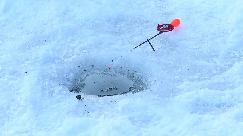 Ice fishing setup with a small rod and reel resting beside a drilled hole in frozen lake ice during winter