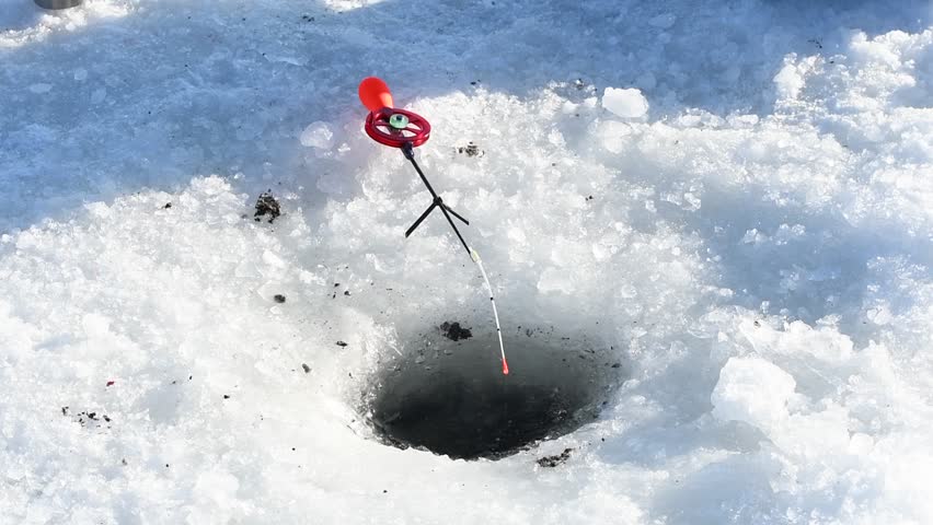 Ice fishing setup with a small rod and reel resting beside a drilled hole in frozen lake ice during winter