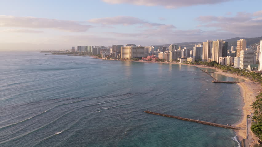 Flying above ocean to reveal Waikiki Beach and city park in Honolulu at sunset