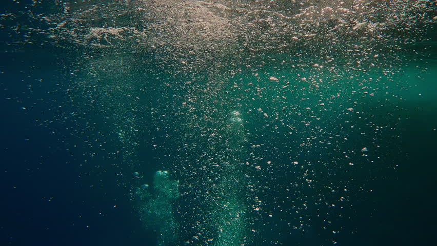 Multitude of air bubbles rise to surface of rippling sea in evening light, illuminated by sun rays. Jets of oxygen bubbles slowly rise to surface in sunlight at sunset. Air bubbles glares at sundown