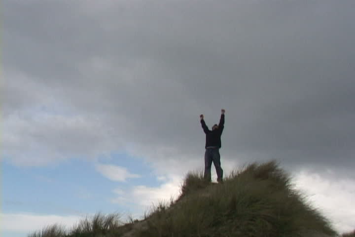 Man on sand dune in Oregon reaches up for the sky.
