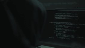 Back view of unrecognizable hooded hacker typing malicious code on computer monitor, accessing private data, performing cyber attack, committing crime, engaging in fraud, working in dark room. - Powered by Shutterstock - Get 15% off with code: PIKWIZARD15