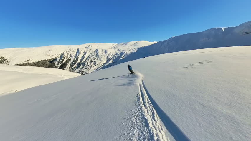 Experienced Skier Enjoying Freeride Heliskiing Down a Pristine Snowy Mountain Slope on a Sunny Day