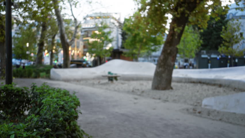 Blurred park scene with soft bokeh and defocused trees, hedge and curved concrete seating in outdoor park; background backplate copyspace calm.