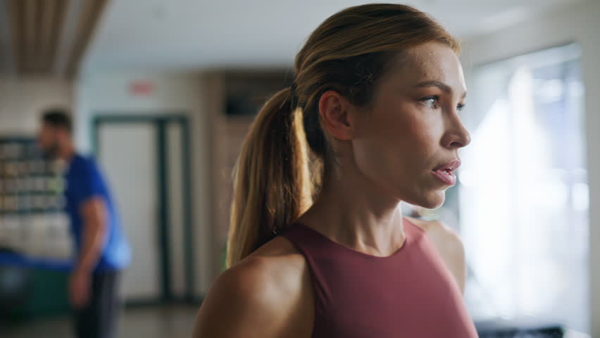 Tired woman drinking water after hard sport training in gym closeup. Portrait exhausted lady athlete refreshing wiping sweat from forehead. Smiling brunette relaxing after energetic cardio workout.
