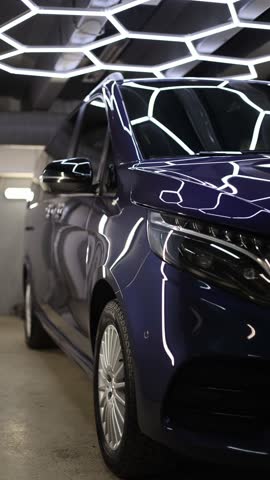 Vertical screen professional car detailing scene showing shiny minivan under ceiling lights inside detailing studio after polishing and ceramic coating with clean reflections premium automotive service atmosphere