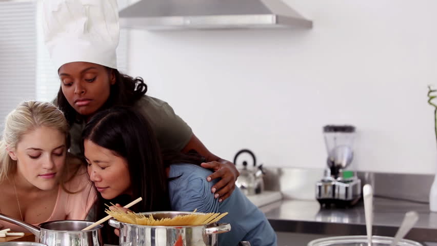 African-american Woman wearing a chef hat and smelling a meal with friends in the kitchen