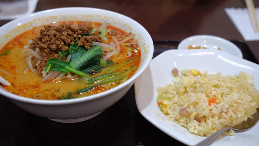 Savor the vibrant colors and textures of a steaming bowl of Tantanmen ramen topped with fresh green onions, crispy crumbles, and in a rich, spicy broth. Close-up shot, rich details.