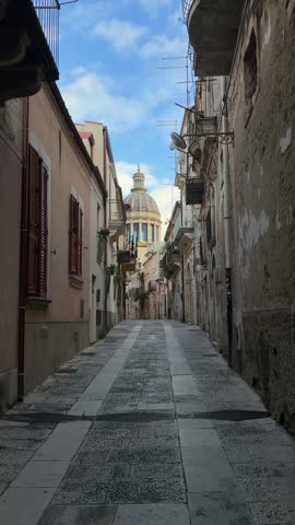 Narrow European street with historic buildings and distant dome view