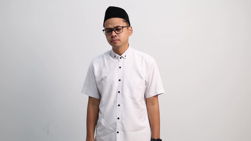 Muslim man wearing a peci with a sad expression because he has a cough while holding his chest.