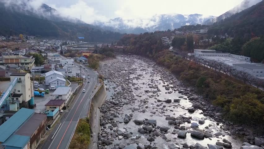 Flyover rocky Kiso River at Nagiso, Japan as low cloud fills mtn valley