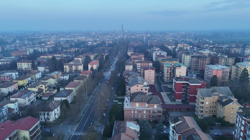Aerial view along Viale Po shows residential neighborhoods of Cremona with the Torrazzo di Cremona and the Duomo di Cremona rising on the skyline under winter haze in Lombardy, northern Italy.
