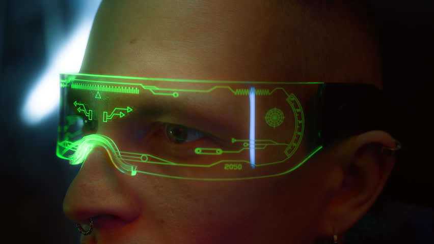 Side close up view of young cyberpunk man with clean-shaven face and piercing, wearing LED smart visor receiving laser scan in dark indoor space