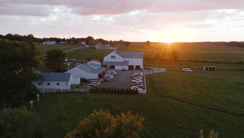 a wonderful view of a sunset from a drone shot of a gorgeous farm and surrounding green pastures and white barn