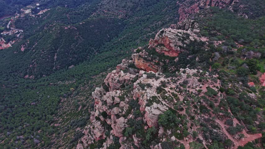 High above the rugged terrain, the cliffs of Spain show rock formations and trees in a green valley. A broad view of the mountains reveals the beauty of nature in this region.