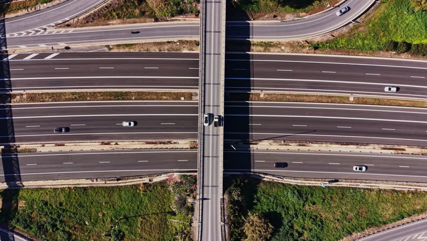Vehicles move on highways and under overpasses in Spain. Lanes are busy with cars traveling in various directions. Green areas are visible near the roads, showing nature.