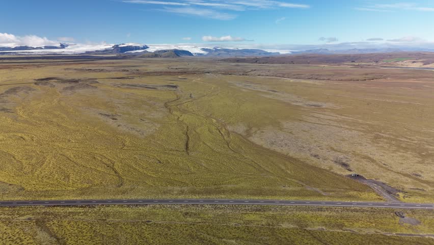 Road in Iceland. Cars are driving along the road. In the background mountains, a glacier, sky, clouds. 4K. Drone