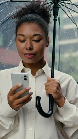 African American business woman with umbrella browsing mobile phone in rainy downtown smiling happy reading good news businesswoman female girl with smartphone enjoy using online app in rain weather