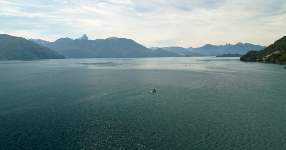 Aerial view over Lago Todos los Santos near Petrohué, Chile, with calm water, distant boat wake and mountain range under soft cloud light in wilderness landscape scenery
