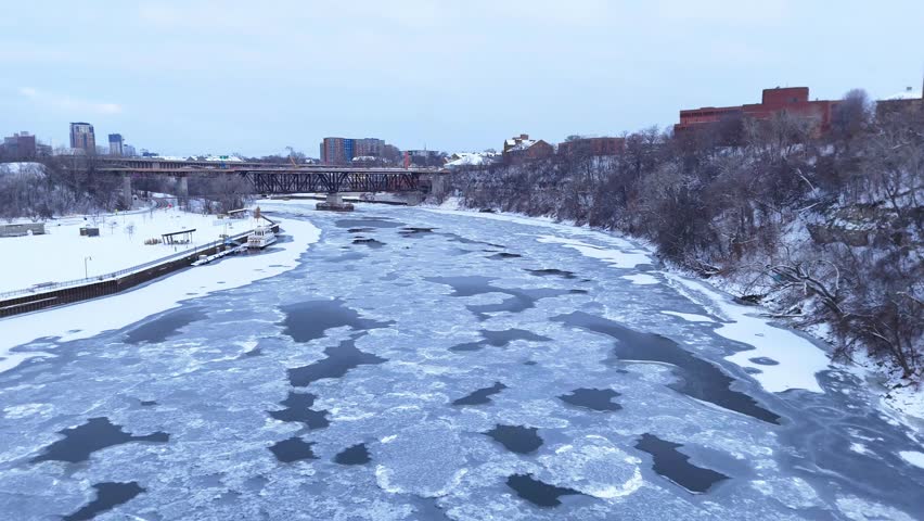 Icy Mississippi River flowing near railroad bridge and Minneapolis city skyline in winter