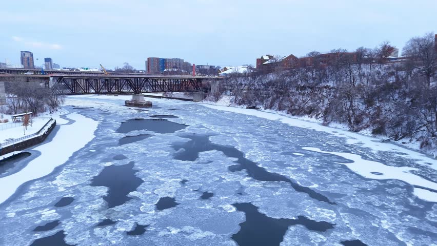 Icy Mississippi River flowing near railroad bridge and Minneapolis city skyline in winter