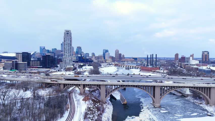 Minneapolis cityscape featuring downtown architecture, I-35W bridge, and a frozen Mississippi River in winter