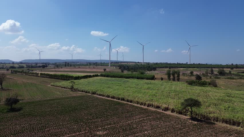 Wind turbine wind farm renewable energy for agriculture on farmland, rural landscape clean energy power generation across green field crop rows under blue sky, horizon, aerial view sunlight
