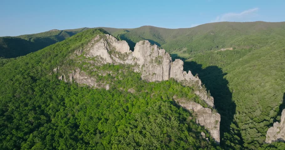 Wide aerial perspective of Seneca Rocks rising above rolling Appalachian terrain, slow ascend