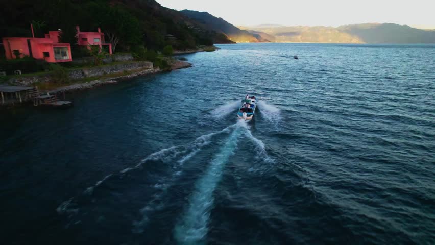 Drone semi orbit following a motorboat near the shoreline of Lake Atitlan with textured water and mountains.
