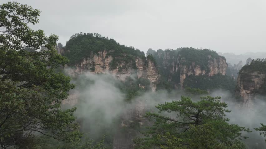A serene view of the mistcovered mountains in Zhangjiajie, China, surrounded by lush greenery. Smooth panning camera movement