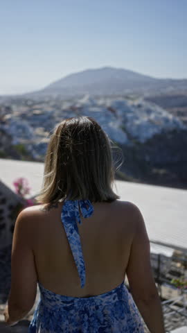 Woman with bare back holding railing looks toward santorini town building viewpoint; serenity travel exploration.