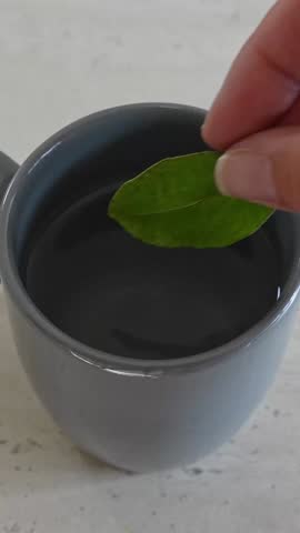 Human hand putting coca leaves into a ceramic mug with hot water. This traditional andean infusion is used as a natural remedy for altitude sickness