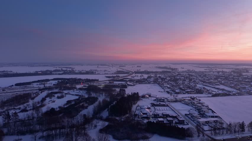 A breathtaking aerial view of a snow-covered landscape at sunset, showcasing serene winter beauty. The vibrant pink sky contrasts with the stillness of the snowy terrain.