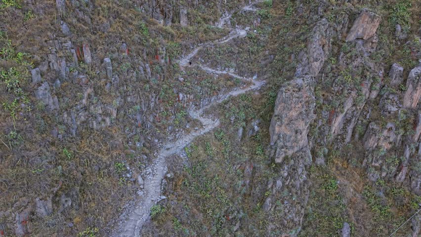 Drone approaches the iconic zigzag hiking trail as a young female traveler descends into Famous Colca Canyon, surrounded by rugged terrain and remote, dramatic landscape.