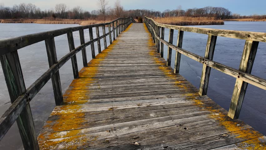 Wooden boardwalk leading over frozen marsh water at Crosswinds Marsh, Michigan in winter, USA