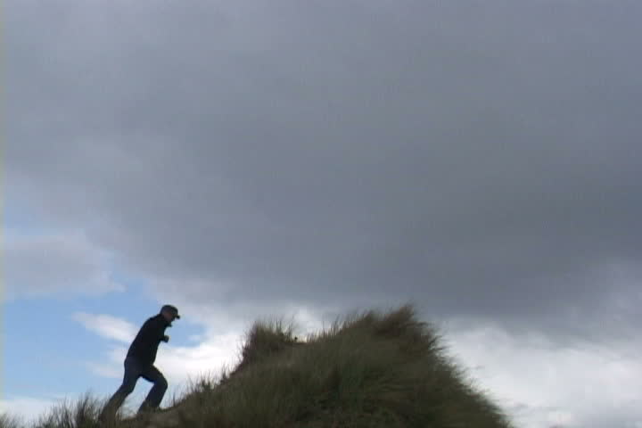 Man runs up sand dune and looks out at the view.
