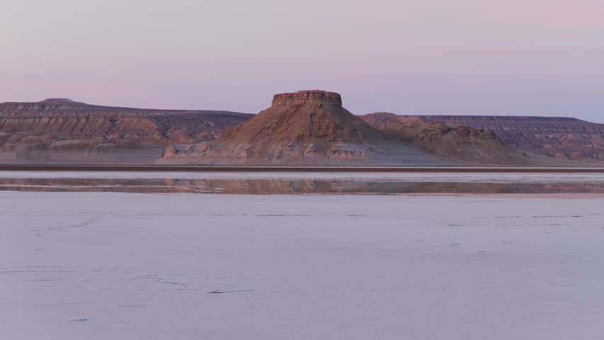 Aerial view of the stark yet stunning landscape, with a table mountain reflecting in a shallow lake, Karynzharyk, Mangystau Region, Kazakhstan.