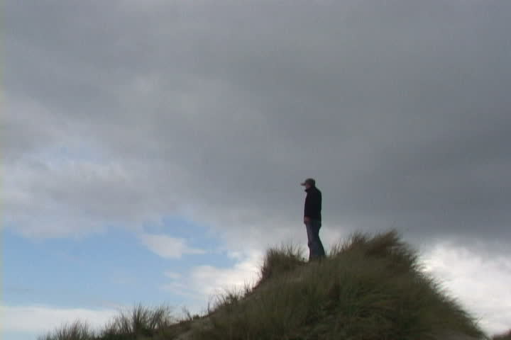 Man on sand dune in Oregon looking out in direction.