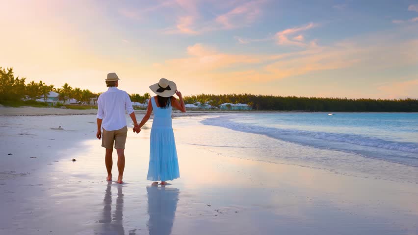 A romantic honeymoon couple walks on a tropical paradise beach and enjoys the beautiful sunset, Bahamas, Caribbean islands