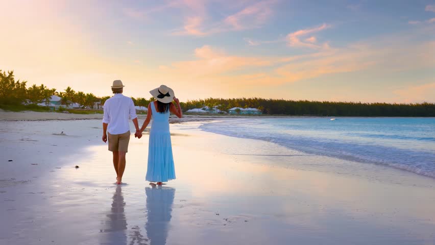 A romantic honeymoon couple walks on a tropical paradise beach and enjoys the beautiful sunset, Bahamas, Caribbean islands