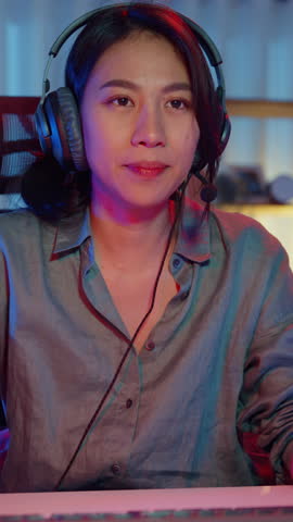 Vertical Screen : Happy asia professional girl gamer wear headphone participation play video game colorful neon lights computer in living room at home. Esport streaming game online, Home activity.