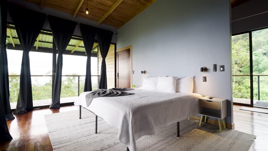 Modern and stylish hotel bedroom interior with large windows and a balcony overlooking a lush green jungle landscape in costa rica