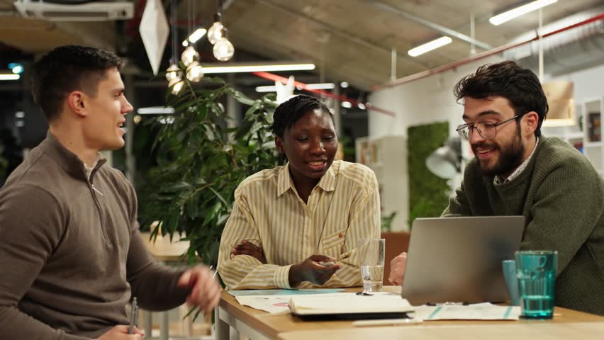 Diverse colleagues collaborating on a business project in a modern coworking space. Young professionals discussing ideas using a laptop