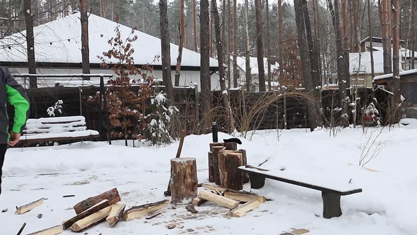 A man chops firewood in the forest near his house