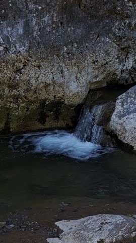 Vertical shot of a small mountain waterfall dropping from a rock into a stream with loud rushing water sound included