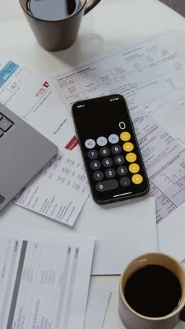 Vertical top view shot of scattered financial documents on coffee table with open computer and calculator