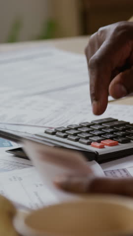 Vertical closeup shot of unrecognizable senior man carefully pressing buttons on calculator while managing personal finances with young woman helping