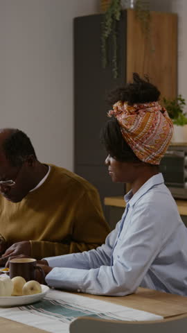 Vertical shot of Black senior man calculating taxes and home finances while sitting at table at home with young woman helping